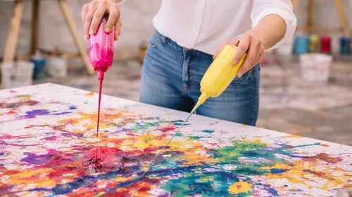 Person gießt bunte Farbe auf Leinwand.