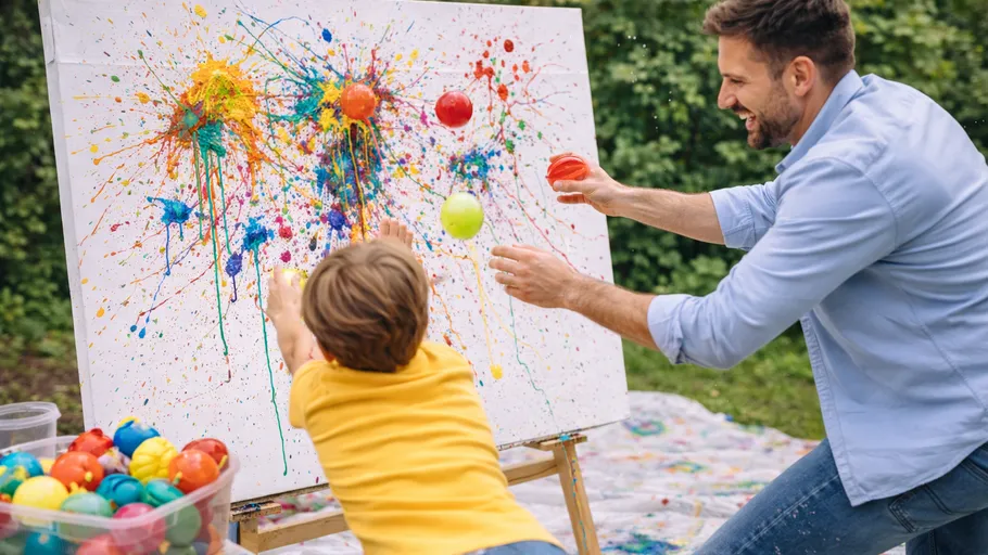 Mann und Kind werfen Farbbälle auf Leinwand.