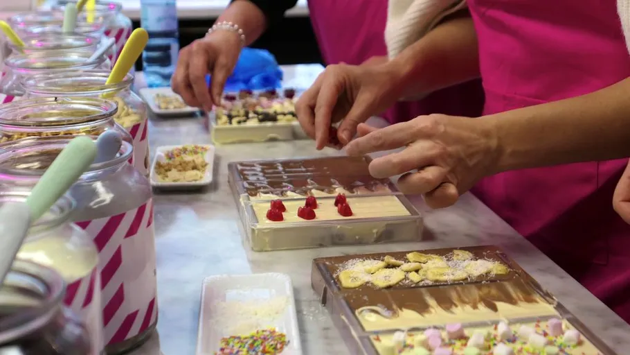 Hands decorate chocolate bars with toppings.