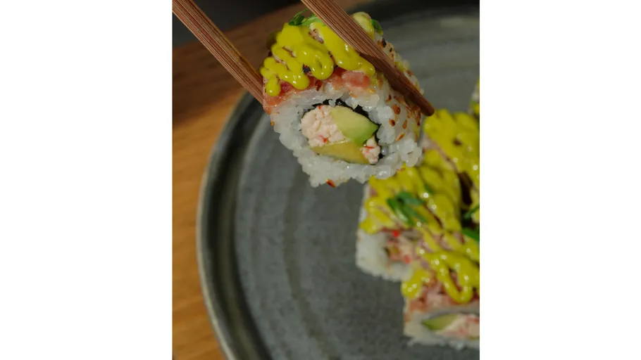 Sushi-Rolle von Stäbchen über Teller gehalten.