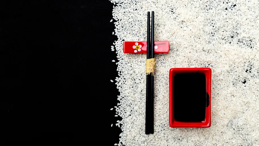 Chopsticks and soy sauce on rice background.
