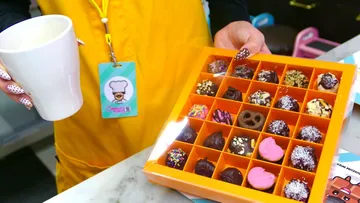 Person hält Pralinen und eine weiße Tasse.