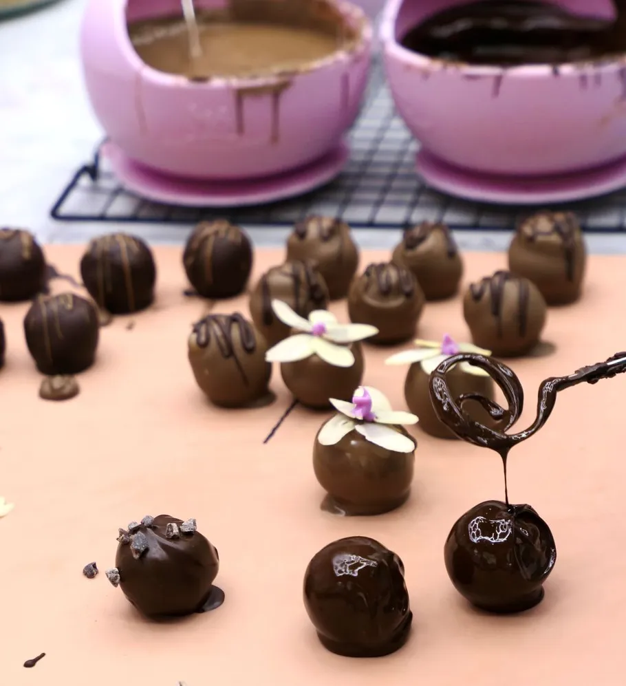 Chocolate truffles being decorated with drizzles.
