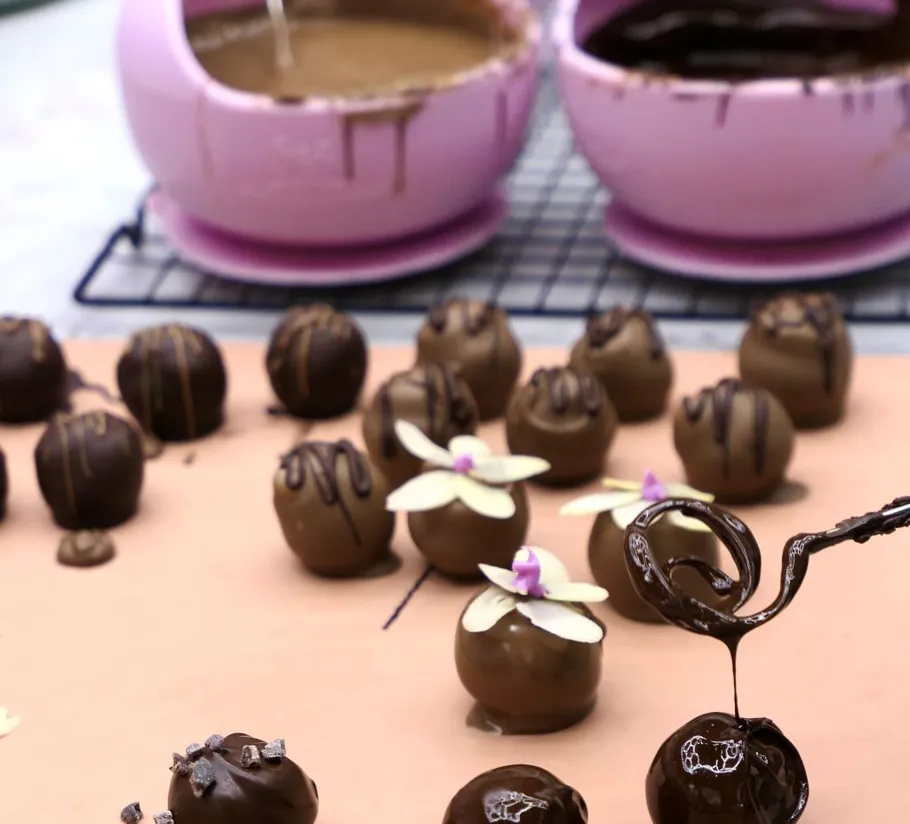 Chocolate truffles being decorated with chocolate drizzle.