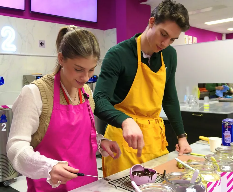 Two people decorating chocolate treats in a kitchen.