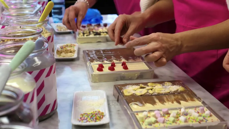 Hands decorating chocolate bars with toppings.