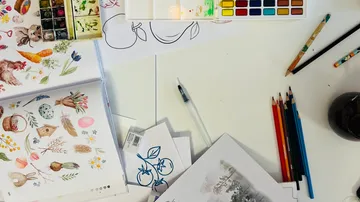 Art supplies and sketches on white table.