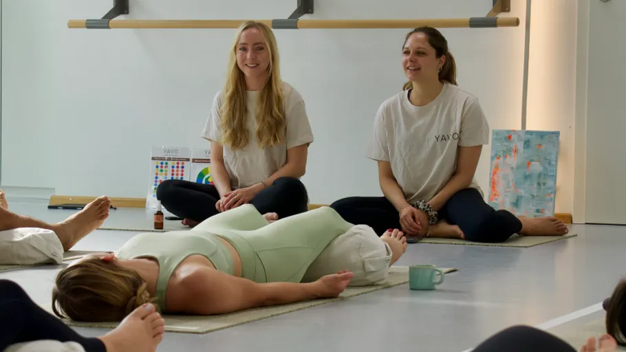 Two women guide yoga class with relaxed participants.