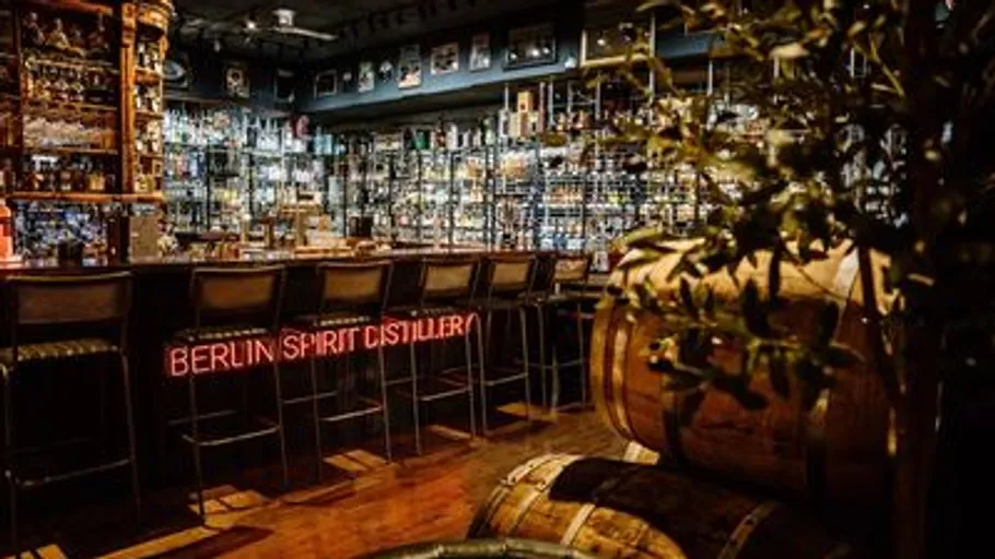 Bar interior with neon sign and barrels.