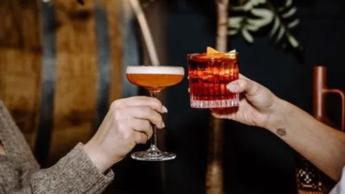 Hands clinking cocktails in dimly lit bar.
