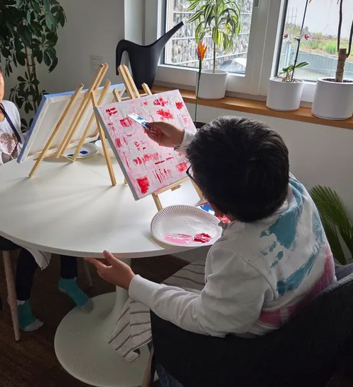 Kinder malen auf Leinwänden in einem Raum.