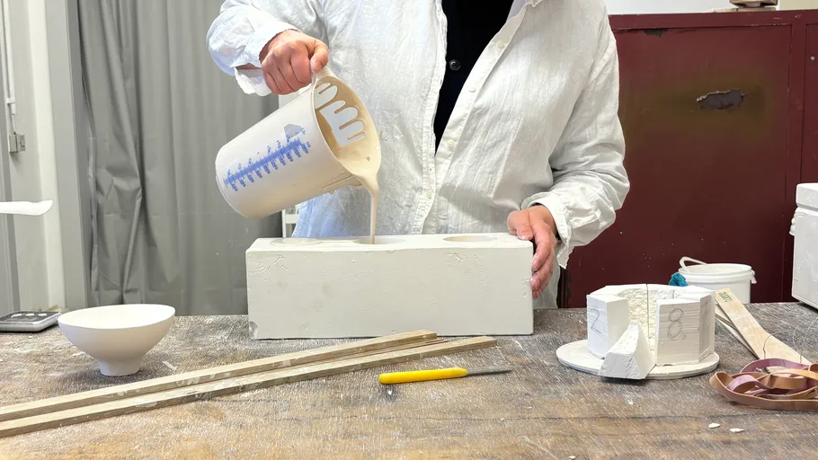Person gießt Flüssigkeit in Form in Werkstatt.