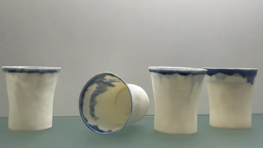 Vier Keramikbecher auf einer reflektierenden Fläche.
