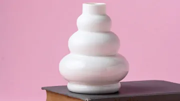 Weiße Vase auf Buch, rosa Hintergrund.