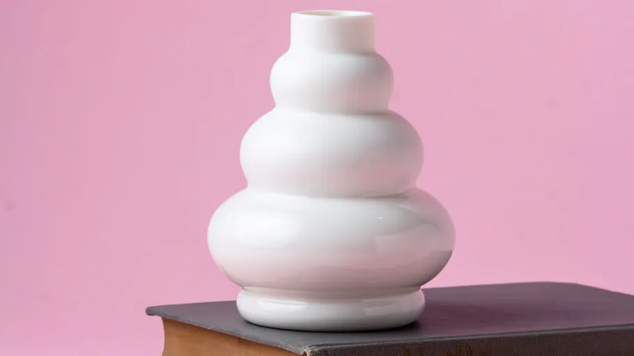 Weiße Vase auf Buch, rosa Hintergrund.