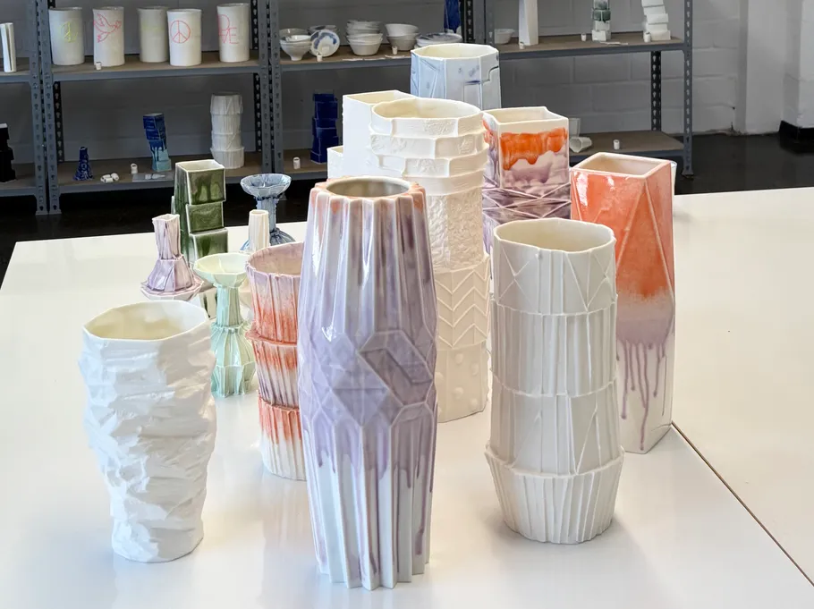 Colorful ceramic vases on white table, shelves behind.