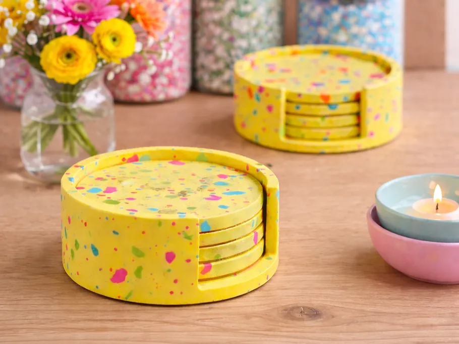 Bunte Untersetzer auf Holztisch, Blumen in der Nähe.