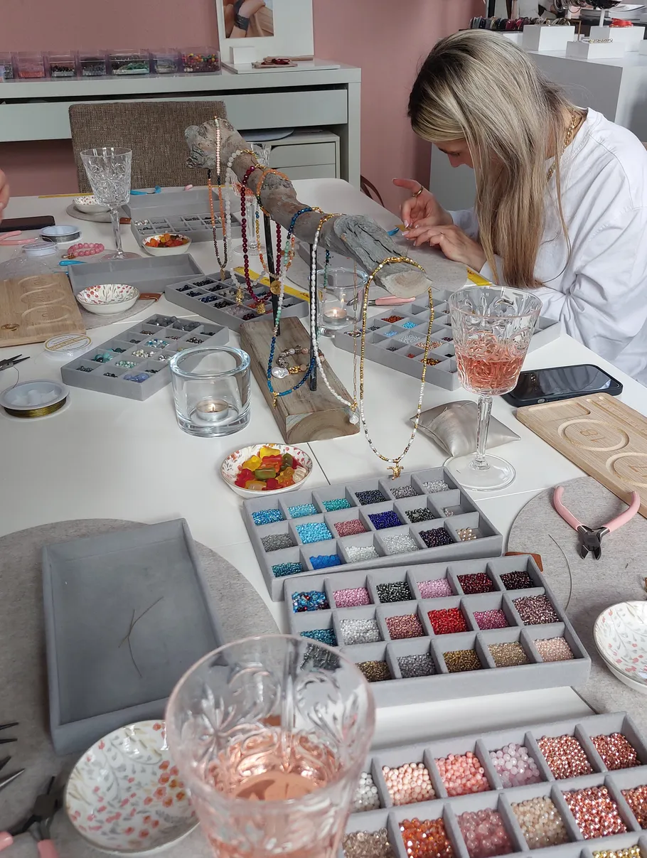 Woman making jewelry with beads on table.