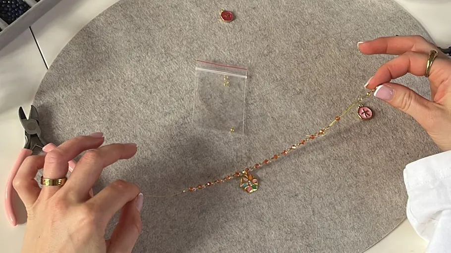 Hands assembling a beaded necklace on table.