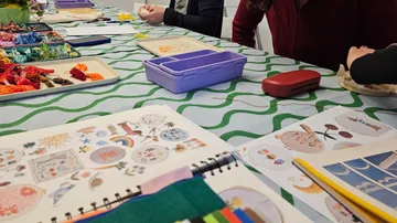 Menschen sticken an einem Tisch mit Materialien.