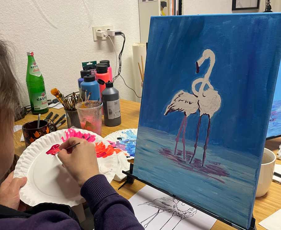 Person painting flamingos on canvas at desk.