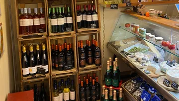Weinflaschen auf Regalen neben Feinkosttheke.