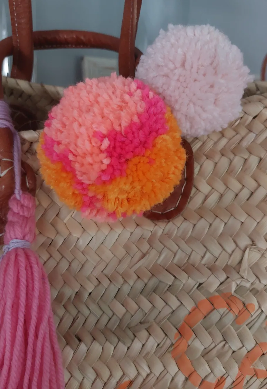 Colorful pom-poms on a woven straw bag.
