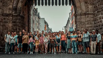 Gruppe von Menschen posiert unter steinernem Torbogen.