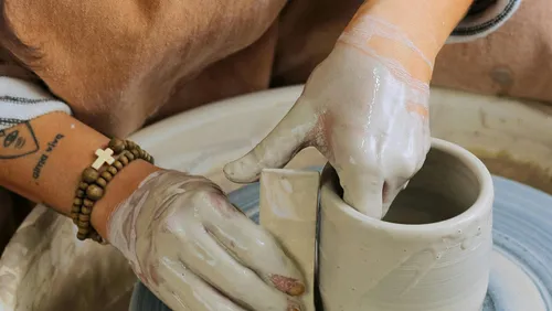 Hands shaping clay mug on pottery wheel.