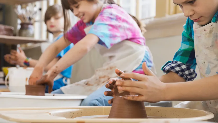 Children shaping clay on pottery wheels indoors.