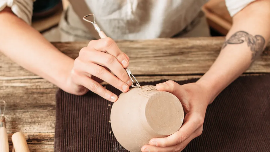 Person carving pottery on a wooden table.