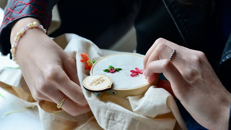 Hands embroidering fabric with colorful flowers.