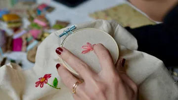 Hand stickt Blumendesign auf Stoffrahmen.