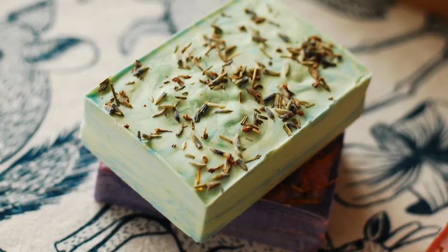 Green soap bar with herbs on fabric.