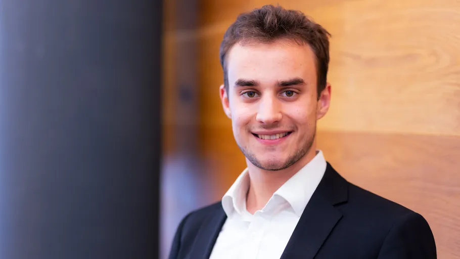 Man smiling in a suit against wooden wall.