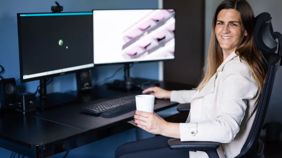 Woman at desk with two monitors smiling.