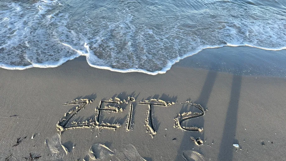 Word 'ZEIT' written on sandy beach.