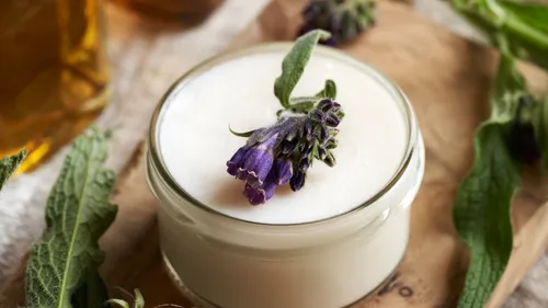 Glas mit Creme und lila Blume.