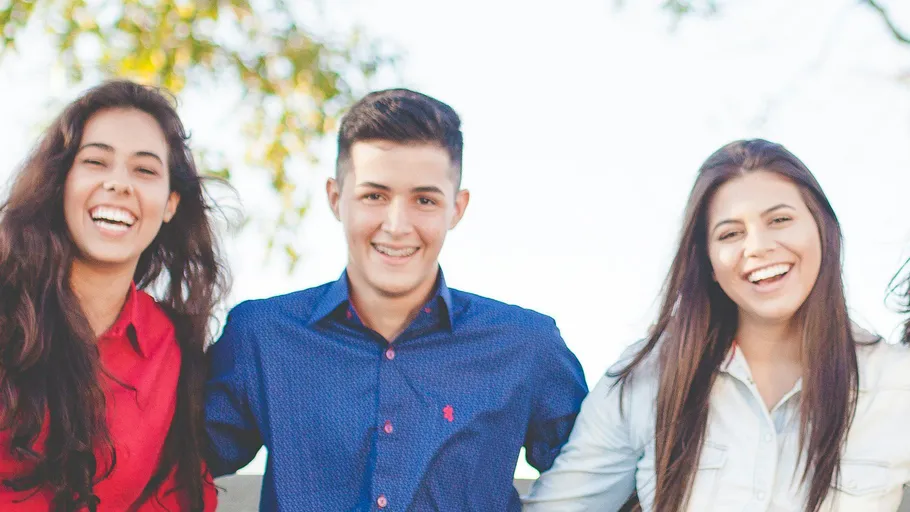 Three friends smiling outdoors in sunlight.