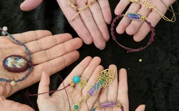 Hands display various handmade jewelry on black background.