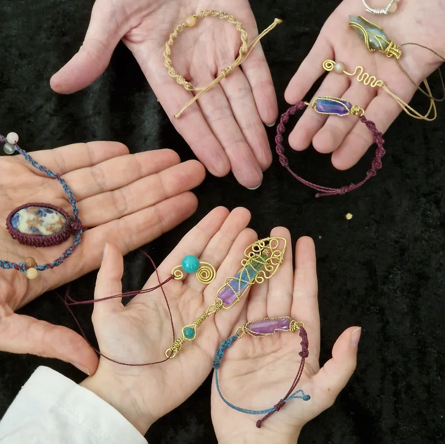 Hands display various handmade jewelry on black background.