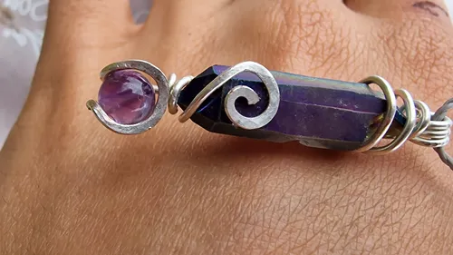 Lila Kristallanhänger auf Hand mit Ringen.