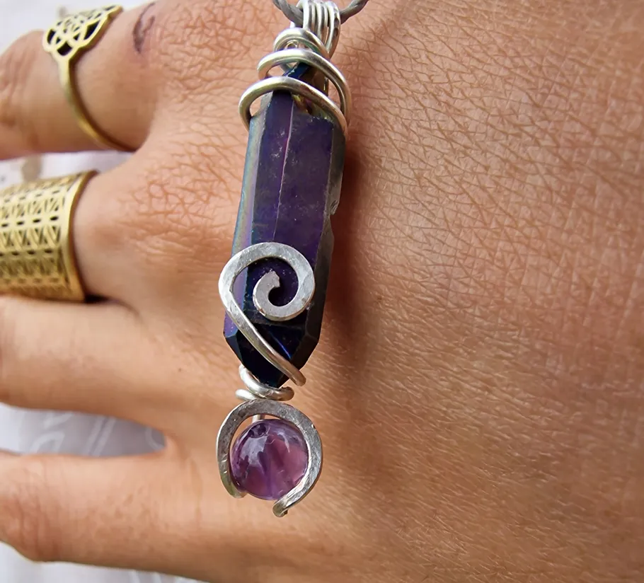 Purple crystal pendant on hand with rings.