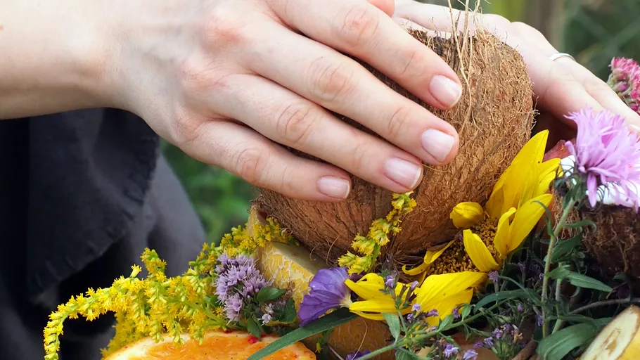 Hände halten Kokosnuss zwischen bunten Blumen.