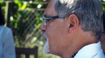 Man with glasses sitting outdoors, side profile.