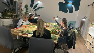 Women create decorations at a large table in a room.