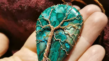 Hand holds teardrop stone pendant with tree design.