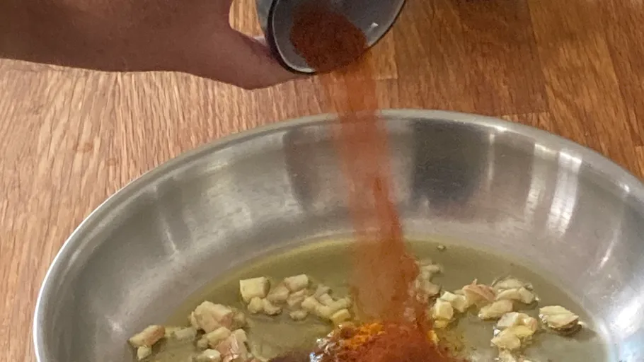 Hand gießt Gewürze in Schüssel auf Tisch.