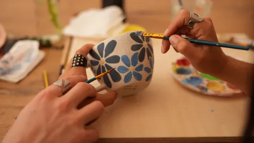 Hände malen Blumenmuster auf Keramikbecher.