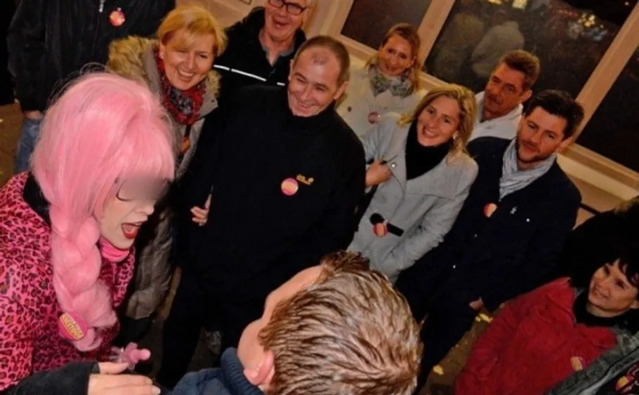 Gruppe von Menschen lächelt eine pinkhaarige Person an.